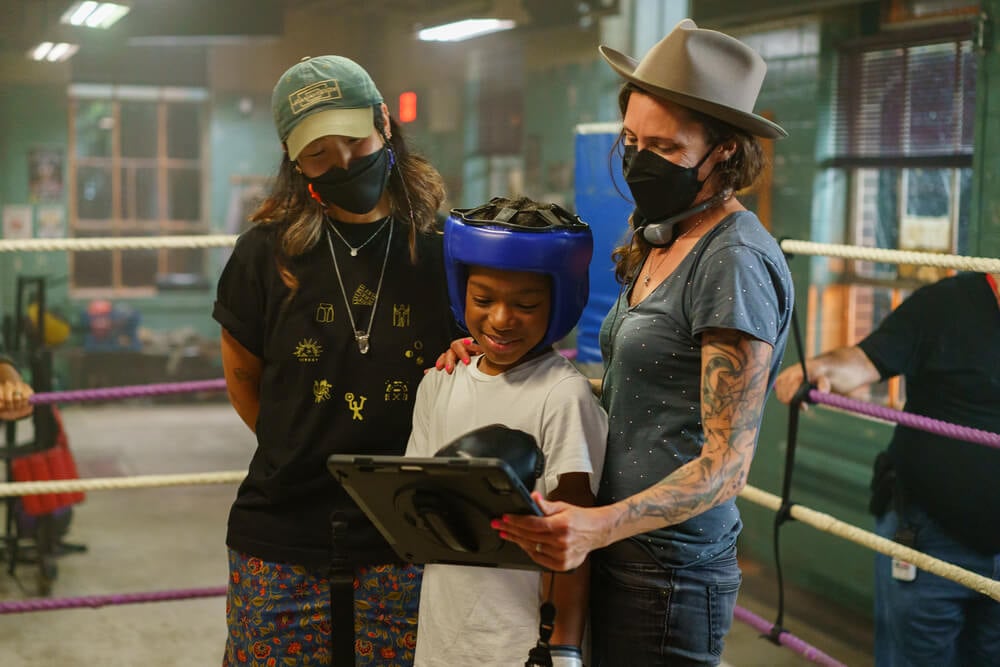 Cinematographer Rina Yang, BSC, (left) and director Rachel Morrison, ASC (right) review footage on a tablet ringside, with a child performer wearing protect headgear