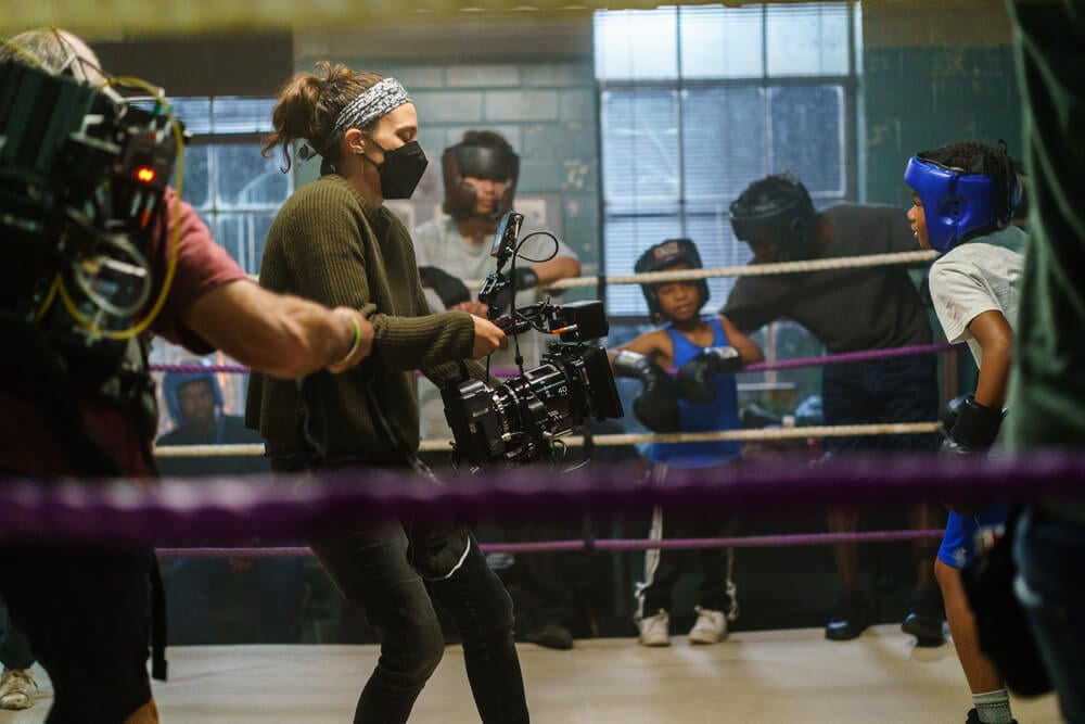 Camera operator films with a Sony Rialto camera rig while boxers train in a boxing ring with natural window light in the background.