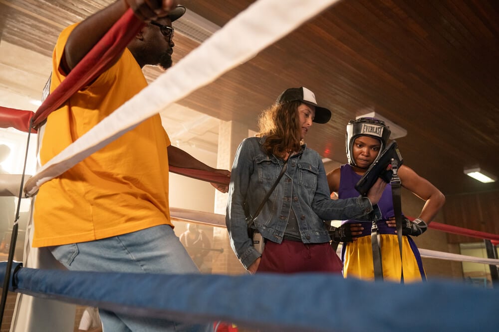 Behind-the-scenes image of director Rachel Morrison, ASC in a denim jacket discussing a shot with lead actors— Ryan Destiny wearing headgear and athletic wear, and Brian Tyree Henry in a boxing ring