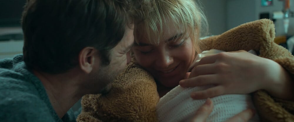 A close-up shot of Alumt (Florence Pugh) and Tobias (Andrew Garfield) embracing a teddy bear together in an intimate moment, captured with soft, cool-toned lighting in the feature 